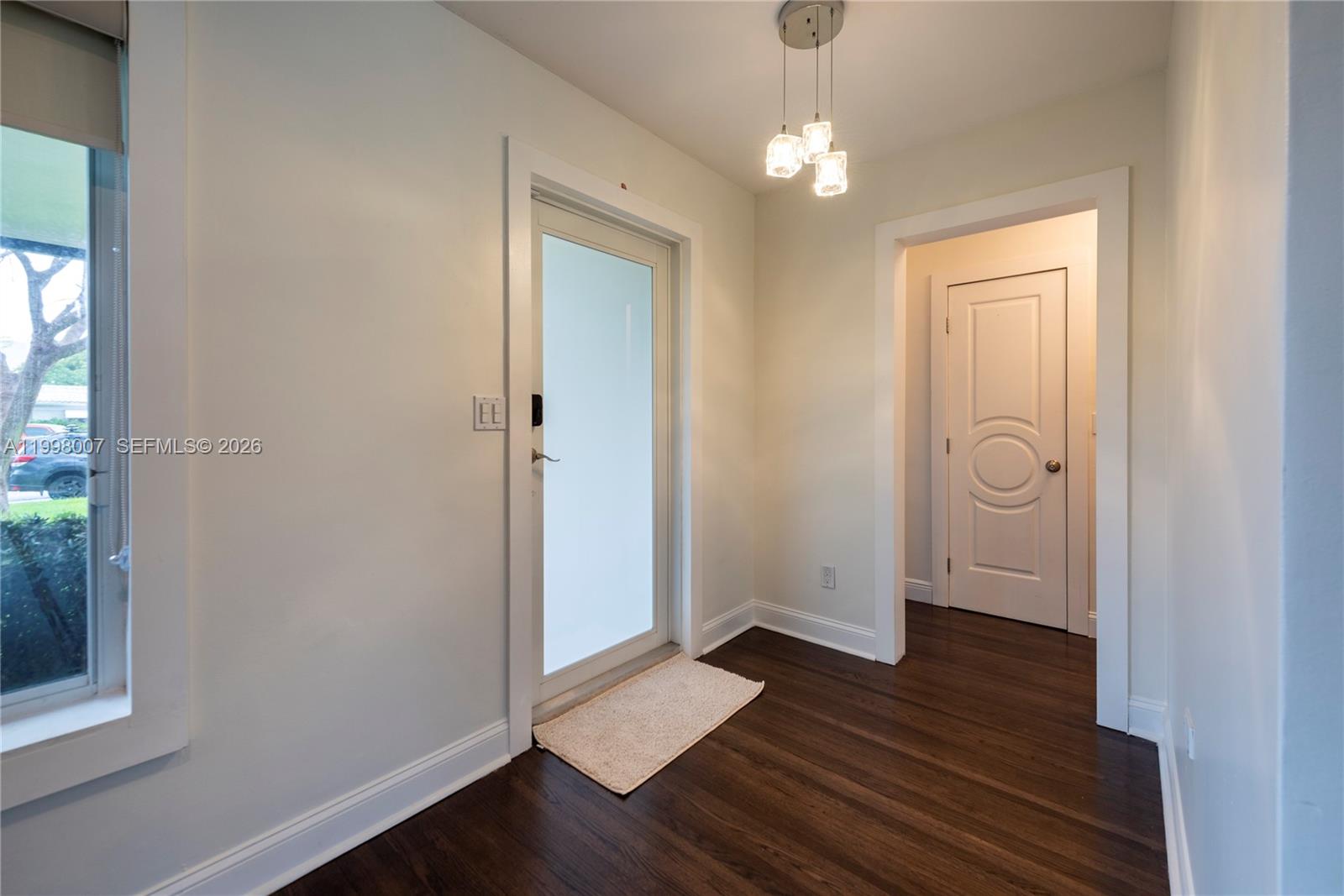 An entryway features dark wood flooring, a glass-paneled door, and a modern pendant light fixture — 3460 Buchanan St, Hollywood FL 33021, HOLLYWOOD, FL