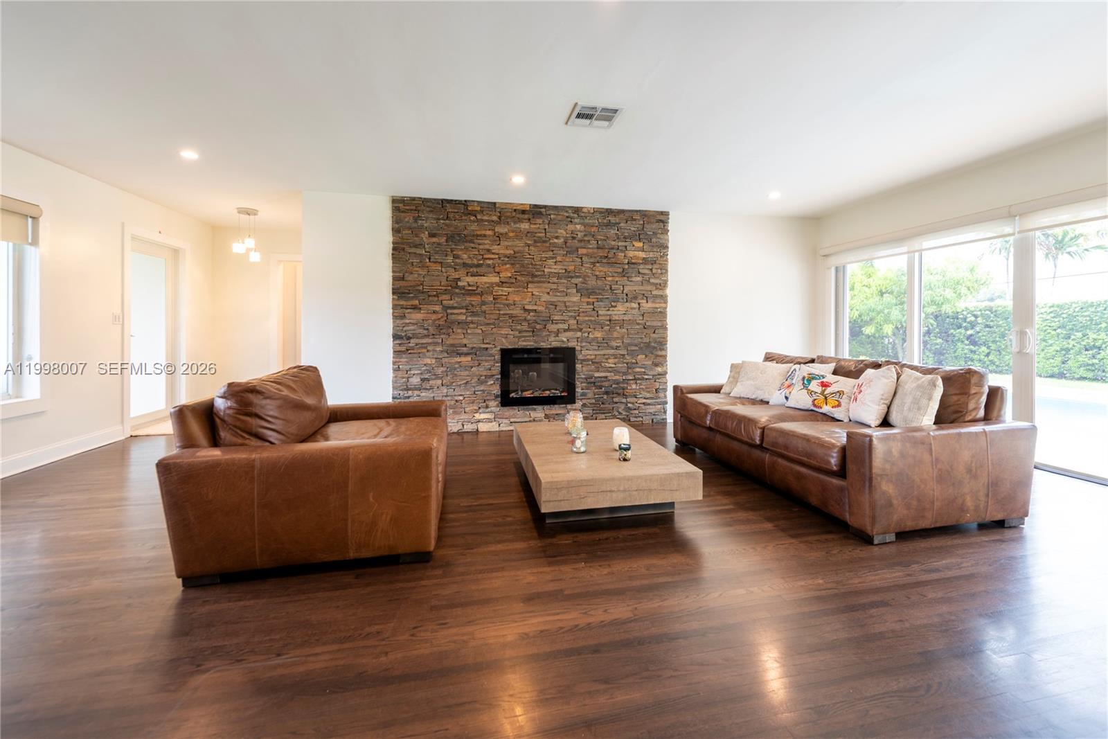 A living room features a stone fireplace, leather furniture, and dark hardwood flooring — 3460 Buchanan St, Hollywood FL 33021, HOLLYWOOD, FL