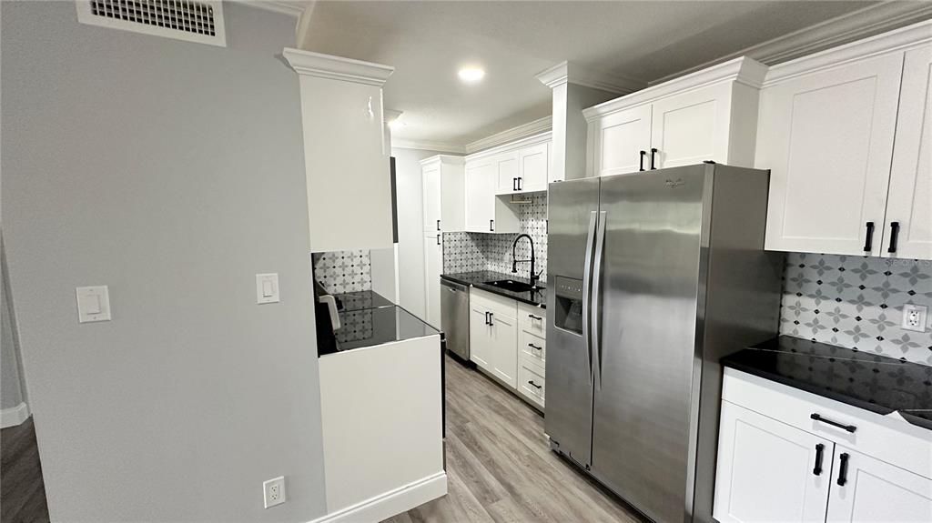 A kitchen features white cabinets, black countertops, stainless steel appliances, and patterned tile backsplashes — 285 WYMORE ROAD UNIT 105, ALTAMONTE SPRINGS, FL