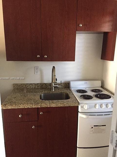A small kitchen features dark wood cabinets, granite countertops, a sink, and a white stove — 371 NE 80th Ter # 12, Miami FL 33138, MIAMI, FL