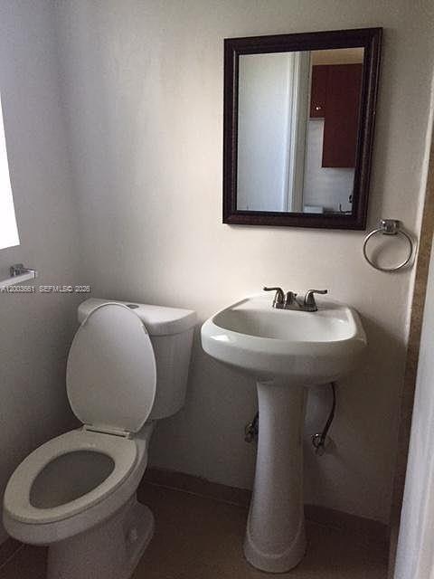 A small bathroom features a white pedestal sink, a toilet, and a framed wall mirror — 371 NE 80th Ter # 12, Miami FL 33138, MIAMI, FL