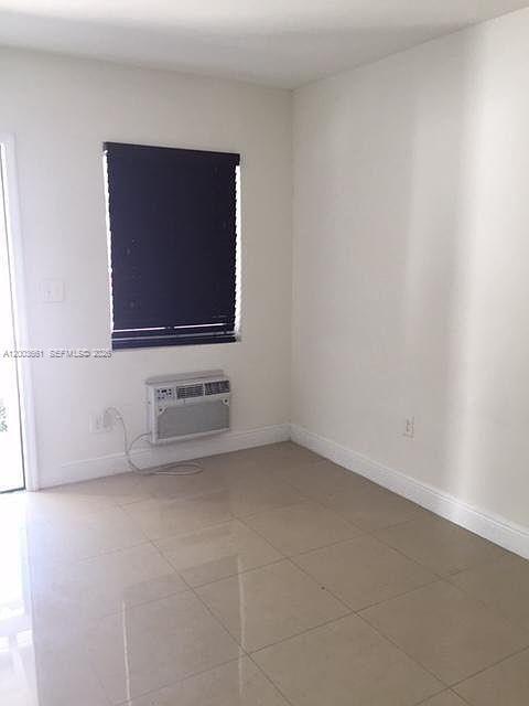 An empty room features light-colored tile flooring, white walls, and a window air conditioning unit — 371 NE 80th Ter # 12, Miami FL 33138, MIAMI, FL