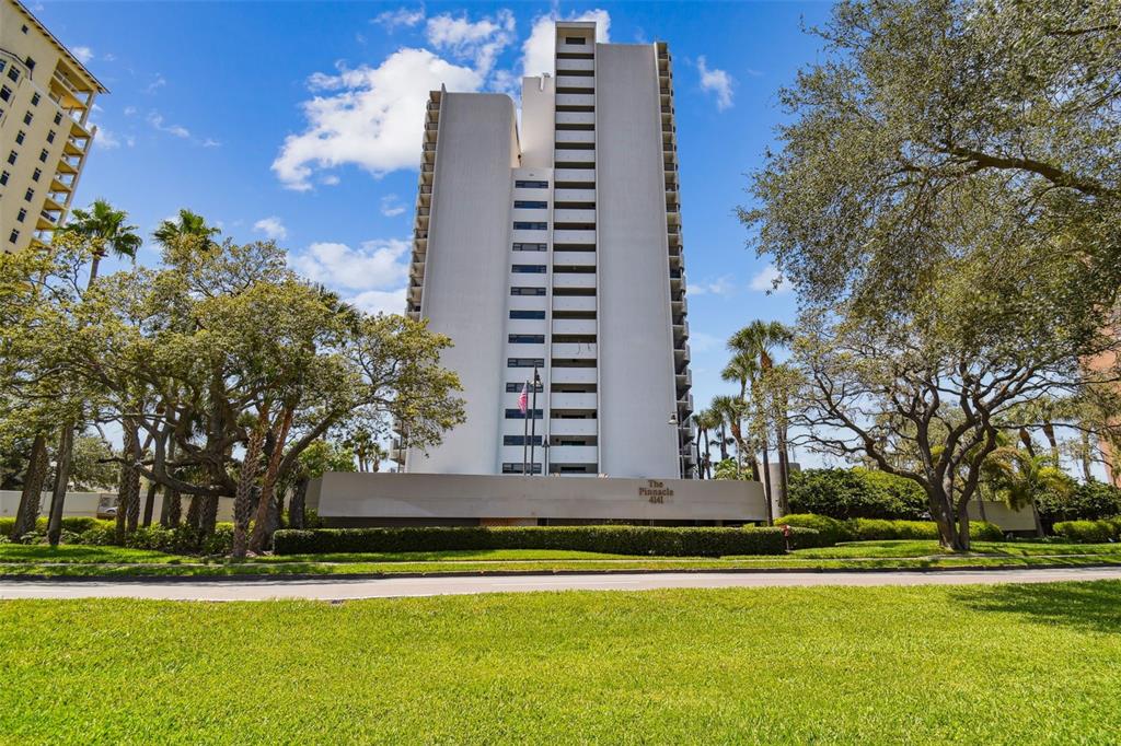 A tall, white residential high-rise building stands behind a green lawn and mature trees — 4141 BAYSHORE BOULEVARD UNIT 1106, TAMPA, FL
