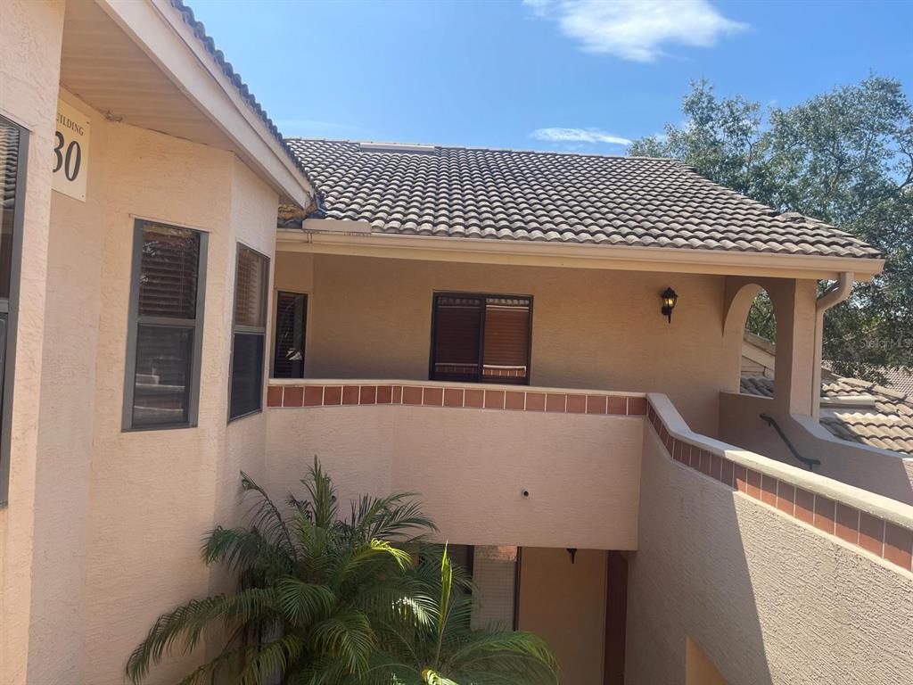 An exterior view of a multi-story stucco building with a tiled roof and palm tree — 7786 SUGAR BEND DRIVE UNIT 7786, ORLANDO, FL
