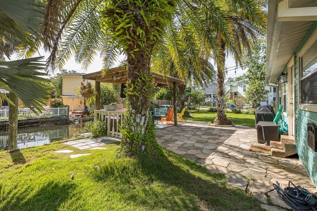 A backyard patio with stone pavers, a wooden pergola, palm trees, and a canal view — 5473 DARLENE STREET, WEEKI WACHEE, FL