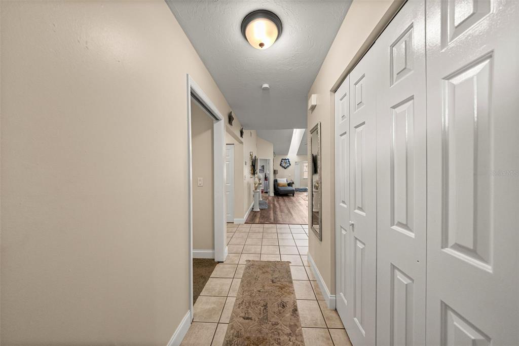 A hallway with tile flooring leads to a living area with wood-look floors — 7799 NE 20TH COURT, OCALA, FL