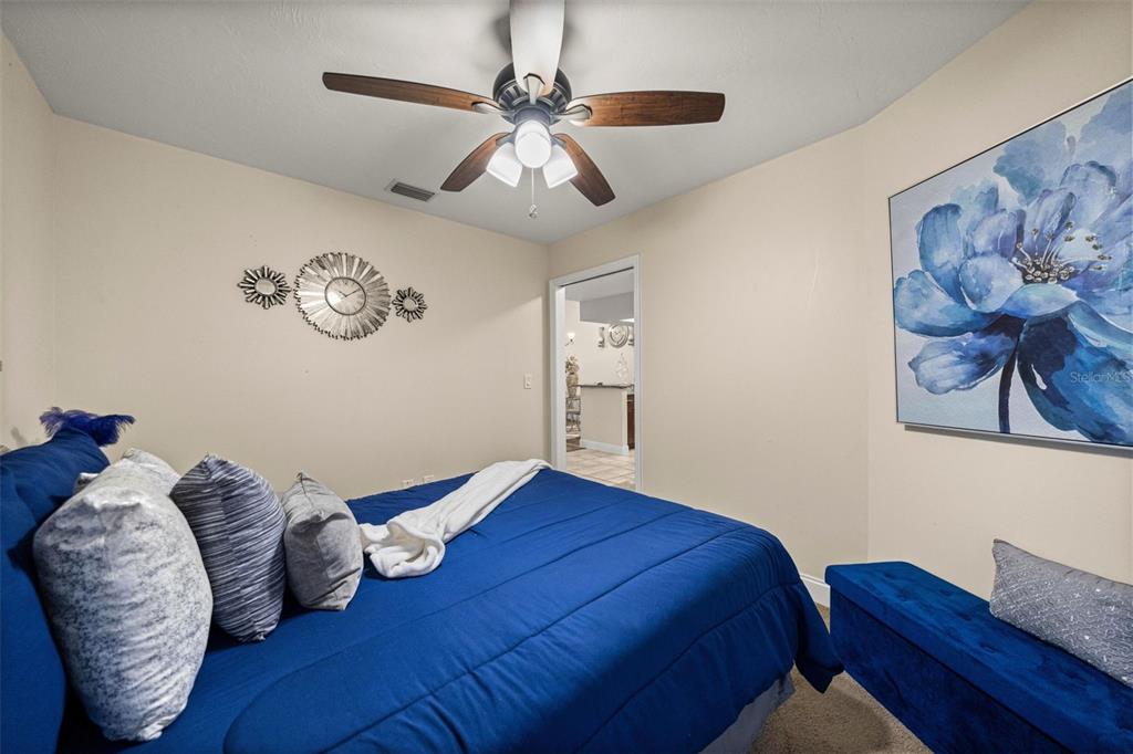 A bedroom features a blue bed, a ceiling fan, and a large floral wall art piece — 7799 NE 20TH COURT, OCALA, FL