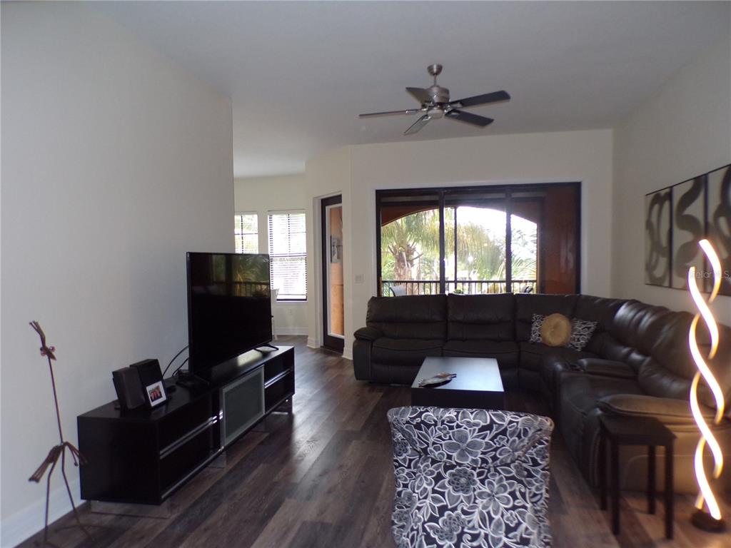 A living room features dark wood-look flooring, a sectional sofa, a television console, and a balcony — 98 VIVANTE BOULEVARD UNIT 9834, PUNTA GORDA, FL