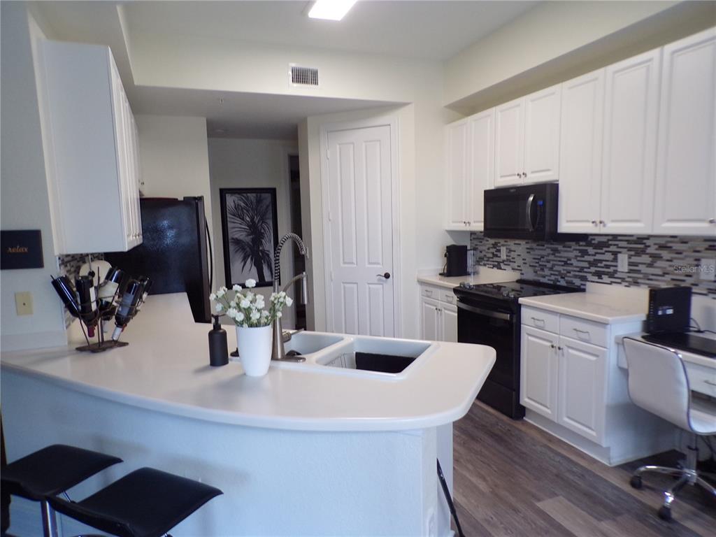 A kitchen features white cabinets, black appliances, a breakfast bar, and a tiled backsplash — 98 VIVANTE BOULEVARD UNIT 9834, PUNTA GORDA, FL