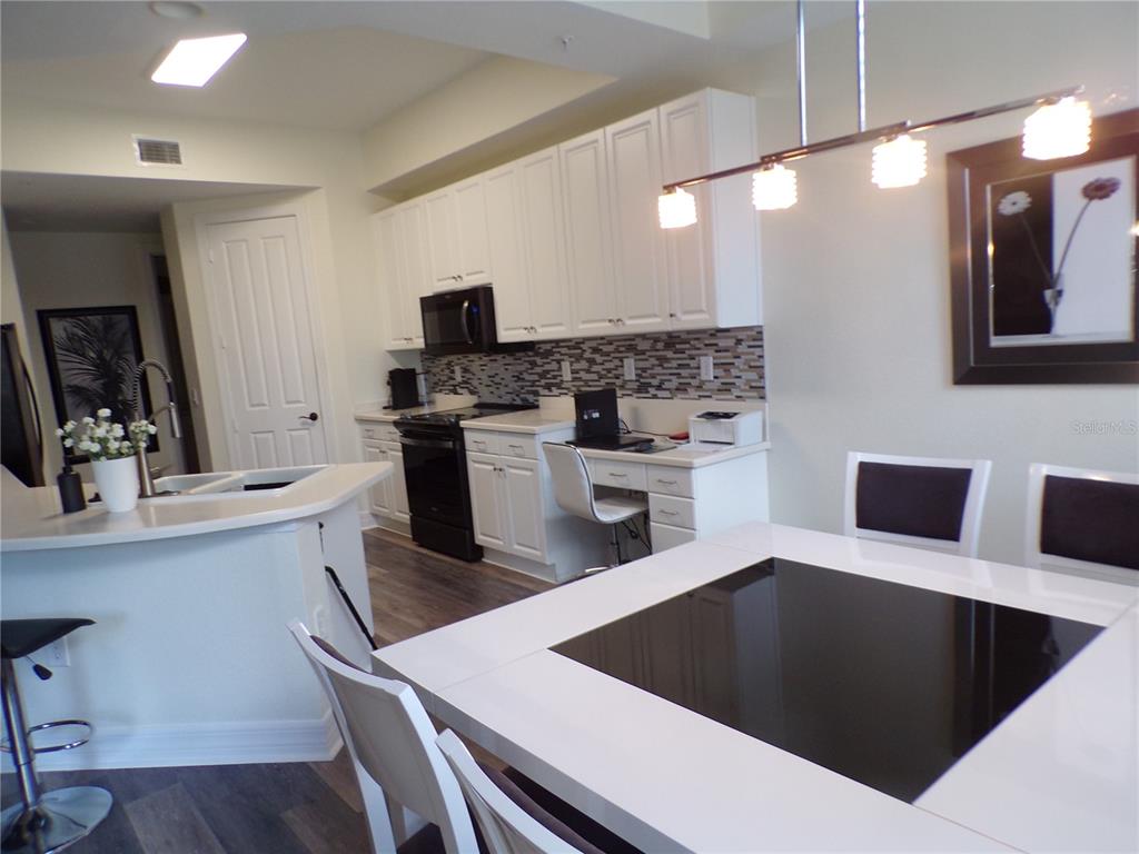 A kitchen features white cabinetry, black appliances, a built-in desk, and a dining table — 98 VIVANTE BOULEVARD UNIT 9834, PUNTA GORDA, FL
