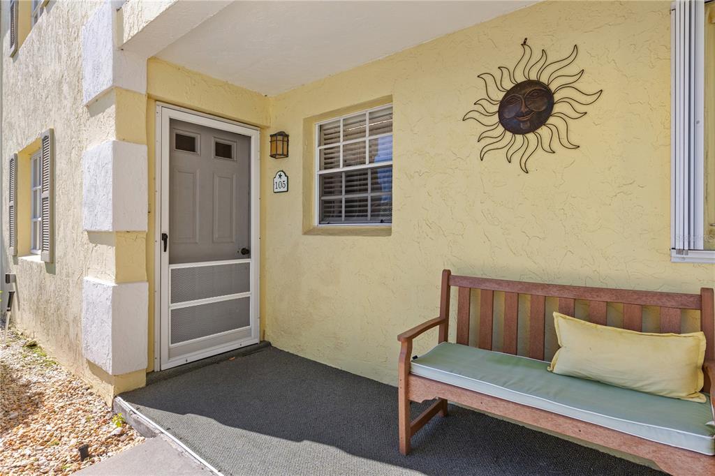 A yellow exterior wall features a front door, a window, and a wooden bench — 942 CAPRI ISLES BOULEVARD UNIT 105, VENICE, FL