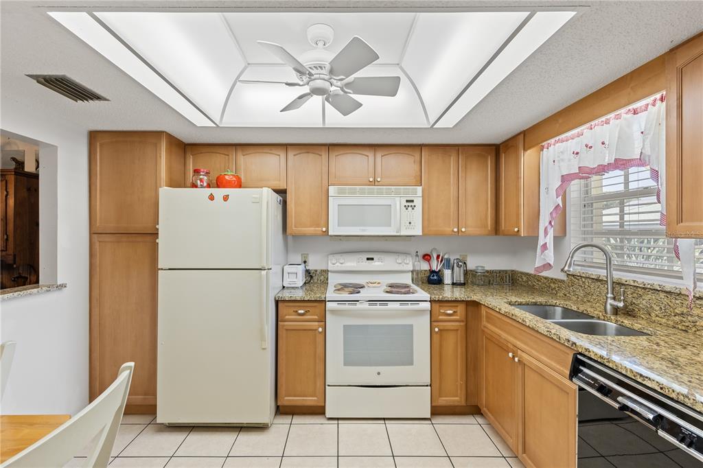 A kitchen features light wood cabinets, granite countertops, white appliances, and a recessed ceiling light — 942 CAPRI ISLES BOULEVARD UNIT 105, VENICE, FL