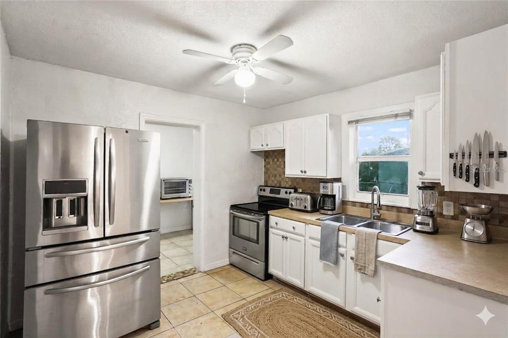 A kitchen with white cabinets, stainless steel appliances, tile flooring, and a ceiling fan — 313 E BOOKER STREET, AVON PARK, FL