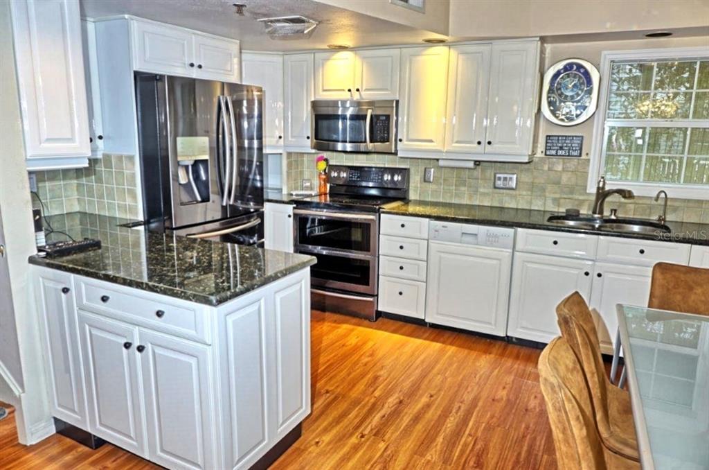 A kitchen features white cabinets, dark granite countertops, stainless steel appliances, and wood-look flooring — 2051 VISTA DEL SOL CIRCLE UNIT 201, LUTZ, FL
