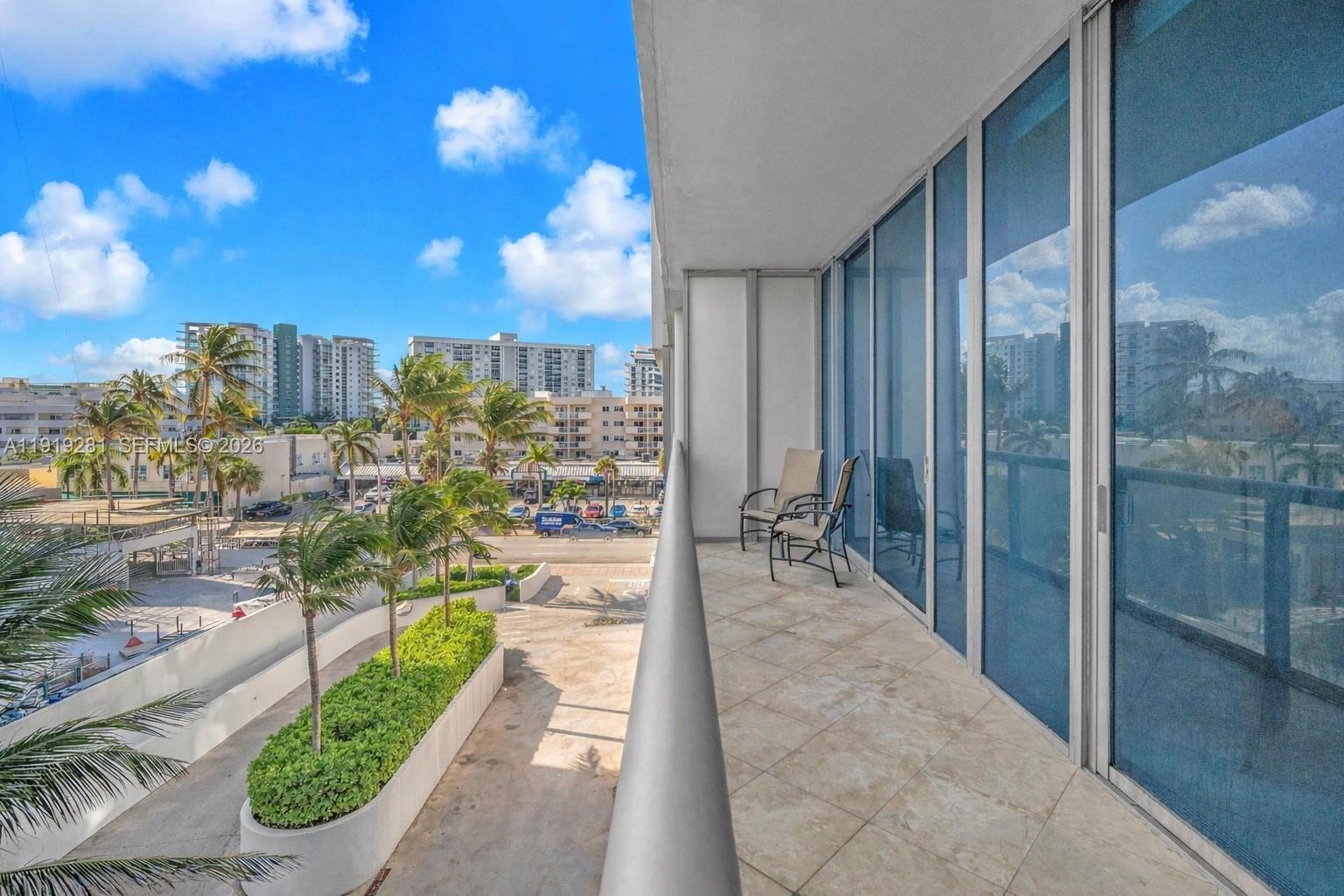 A balcony with tile flooring and two chairs overlooks a street with palm trees — 6799 Collins Ave # 309, Miami Beach FL 33141, MIAMI BEACH, FL