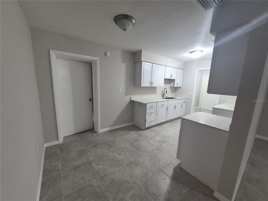 A kitchen features white cabinets, light countertops, gray tile flooring, and neutral wall paint — 15 N WASHINGTON STREET, BEVERLY HILLS, FL