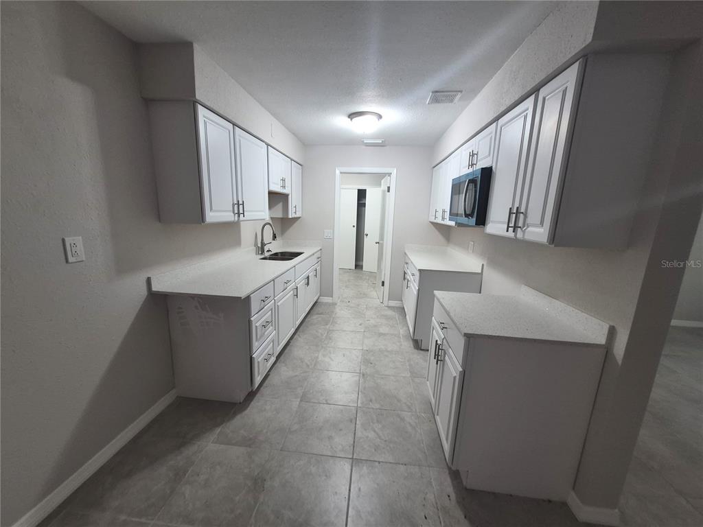 A galley kitchen features white cabinets, light countertops, and gray tile flooring — 15 N WASHINGTON STREET, BEVERLY HILLS, FL