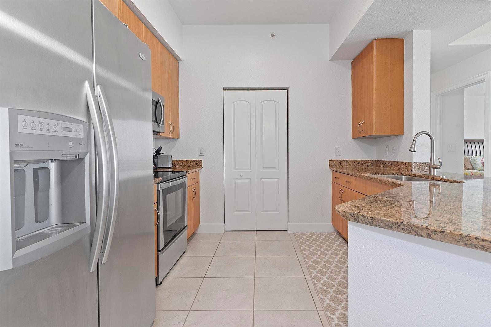 A kitchen features stainless steel appliances, light wood cabinets, granite countertops, and tile flooring — 1830 Radius Drive # 1219, Hollywood FL 33020, HOLLYWOOD, FL