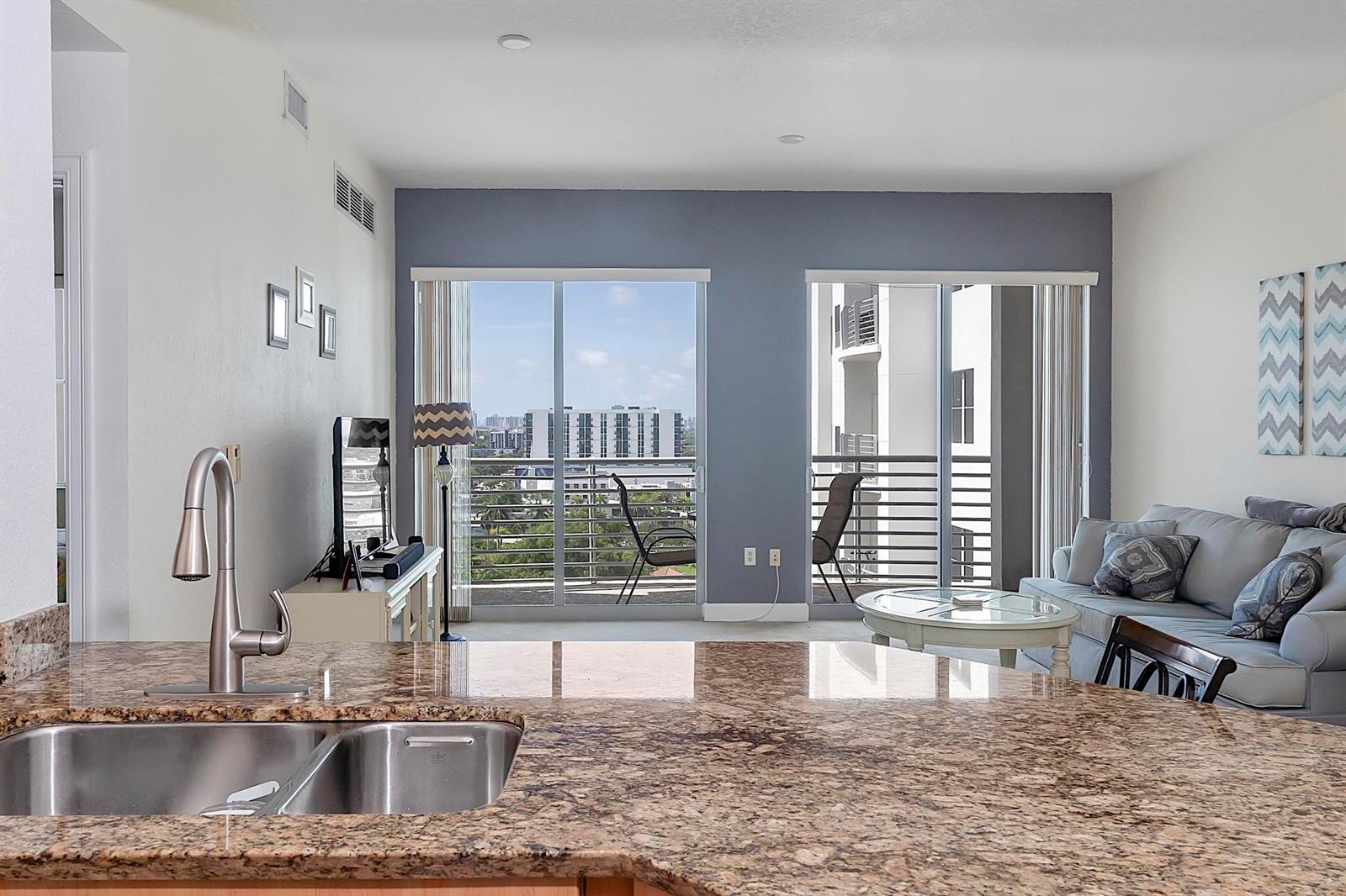 A kitchen island with a granite countertop overlooks a living room with a balcony view — 1830 Radius Drive # 1219, Hollywood FL 33020, HOLLYWOOD, FL