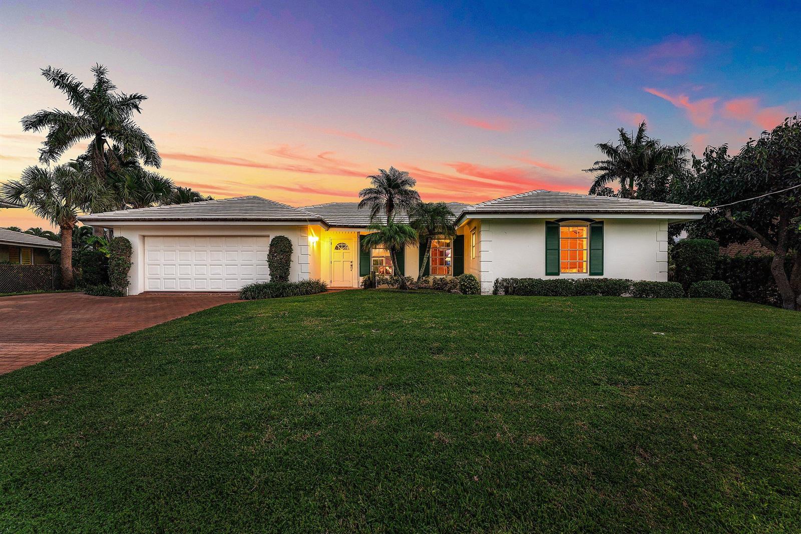 A single-story white house with a two-car garage and green shutters at sunset — 23 Sabal Island Drive, Ocean Ridge FL 33435, OCEAN RIDGE, FL