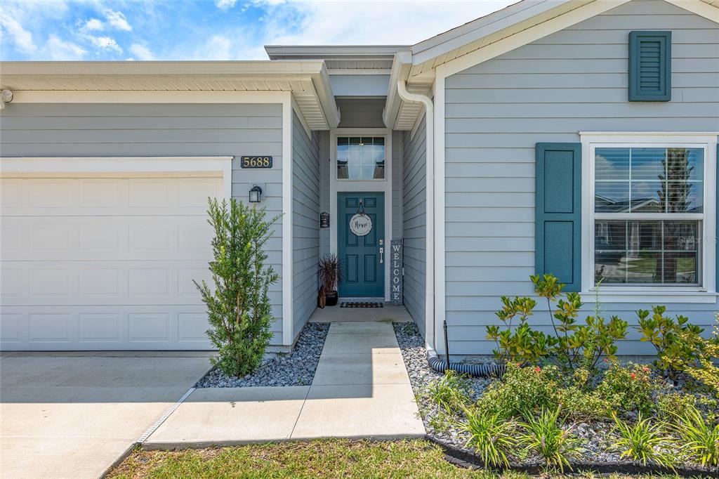 The exterior of a light blue house features a white garage door and teal front door — 5688 SW 92ND PLACE, OCALA, FL