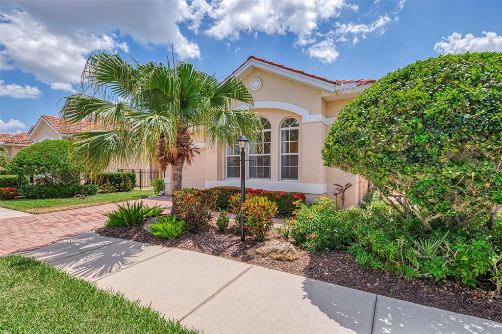 A single-story house with a tan stucco exterior, tile roof, and landscaped front yard — 7803 33RD STREET E, SARASOTA, FL
