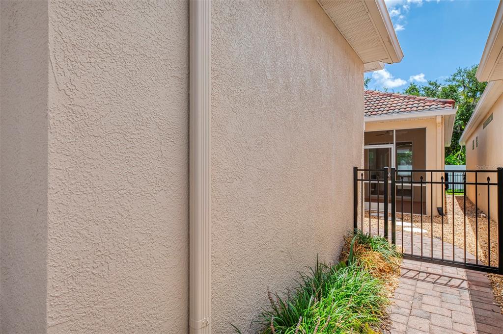 A beige stucco exterior wall with a downspout next to a metal gate and walkway — 7803 33RD STREET E, SARASOTA, FL