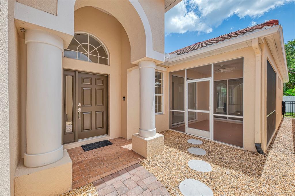 A front entrance with a brown door, white columns, and an adjacent screened-in porch area — 7803 33RD STREET E, SARASOTA, FL