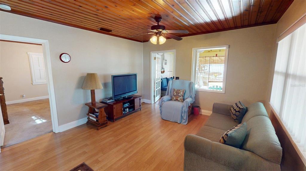 A living room features a wood-paneled ceiling, light wood flooring, a television, and a sofa — 1405 N LAKE REEDY BOULEVARD, FROSTPROOF, FL