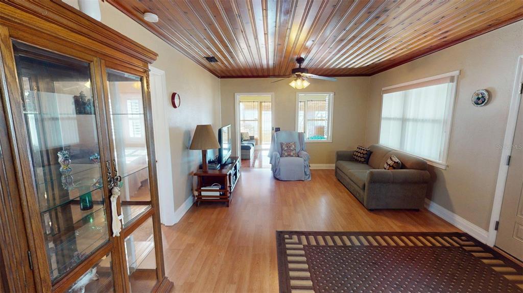 A living room features wood-paneled ceilings, light wood flooring, a sofa, and a glass display cabinet — 1405 N LAKE REEDY BOULEVARD, FROSTPROOF, FL