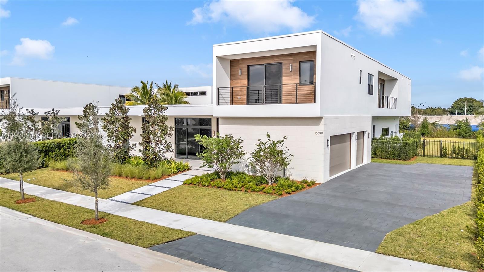 A modern two-story house features white stucco walls, wood-paneled accents, and a paved driveway — 16699 N Botaniko Dr N, Weston FL 33326, WESTON, FL