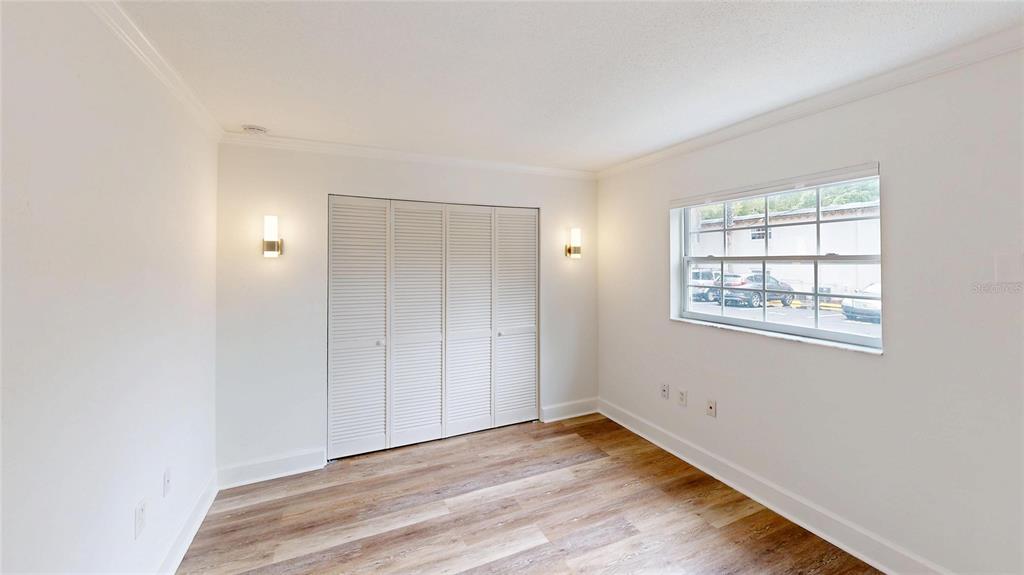 An empty bedroom features white walls, wood-look flooring, a louvered closet, and a window — 2501 E CENTRAL BOULEVARD UNIT 10, ORLANDO, FL