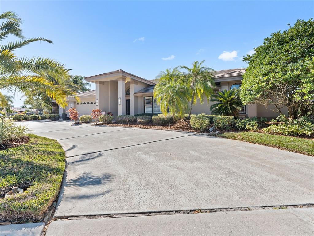 A single-story house with a concrete driveway, palm trees, and landscaping under a blue sky — 4830 LONGWATER WAY, TAMPA, FL