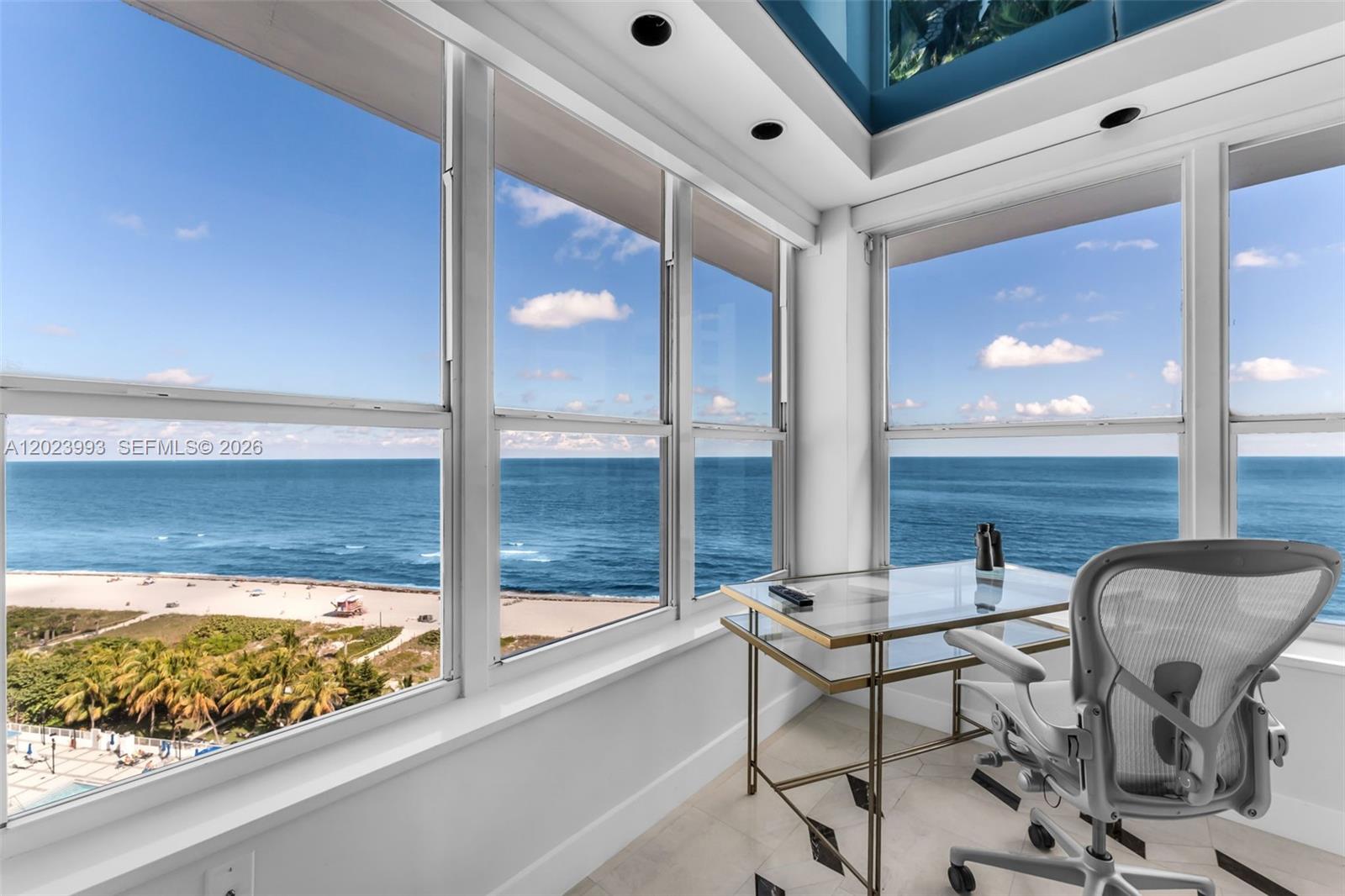 A sunroom with a glass desk and office chair overlooks a beach and the ocean — 4925 Collins Ave # 11E, Miami Beach FL 33140, MIAMI BEACH, FL