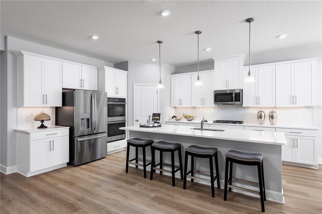 A modern kitchen features white cabinetry, stainless steel appliances, a large island, and wood flooring — 1742 UPLAND LANE, WINTER HAVEN, FL