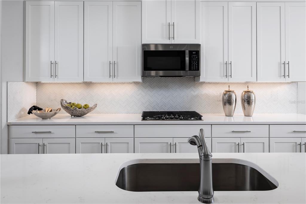 A modern kitchen features white shaker cabinets, a herringbone backsplash, and a stainless steel microwave — 1742 UPLAND LANE, WINTER HAVEN, FL
