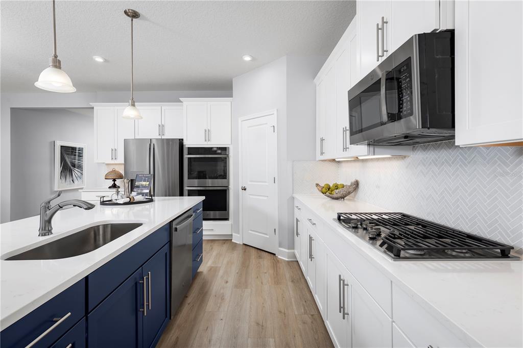 A modern kitchen features white upper cabinets, a blue island, stainless appliances, and herringbone backsplash — 1742 UPLAND LANE, WINTER HAVEN, FL
