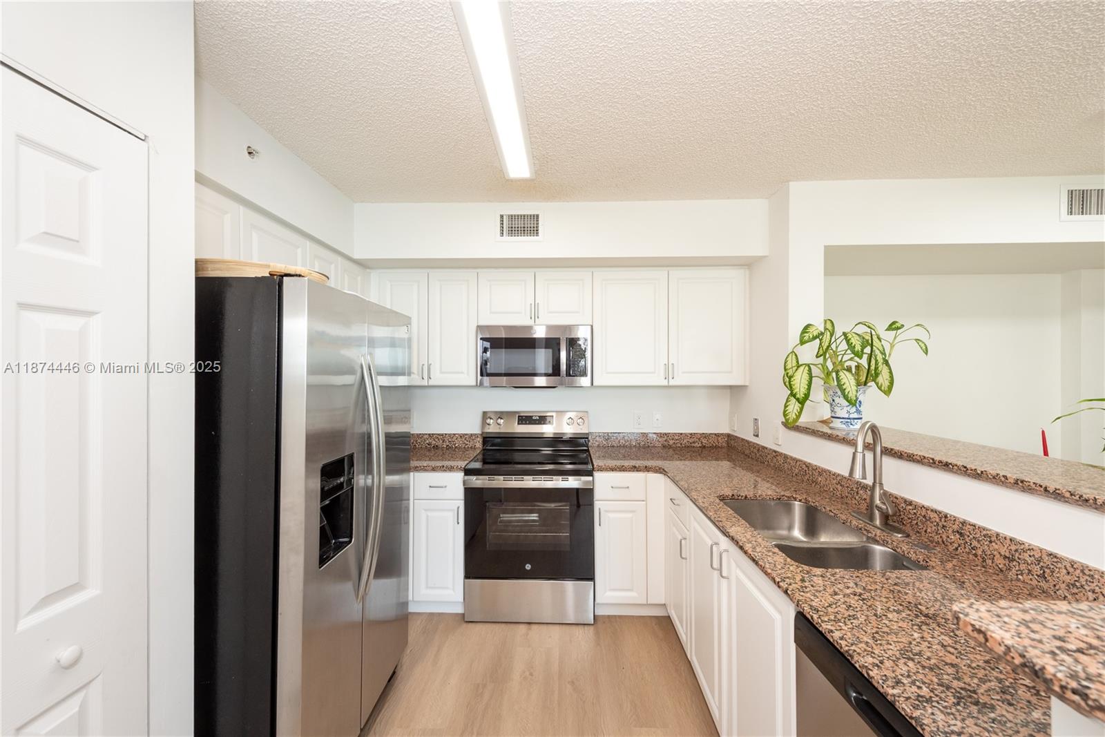 A kitchen features white cabinets, granite countertops, stainless steel appliances, and light wood flooring — 1155 Brickell Bay Dr # 609, Miami FL 33131, MIAMI, FL