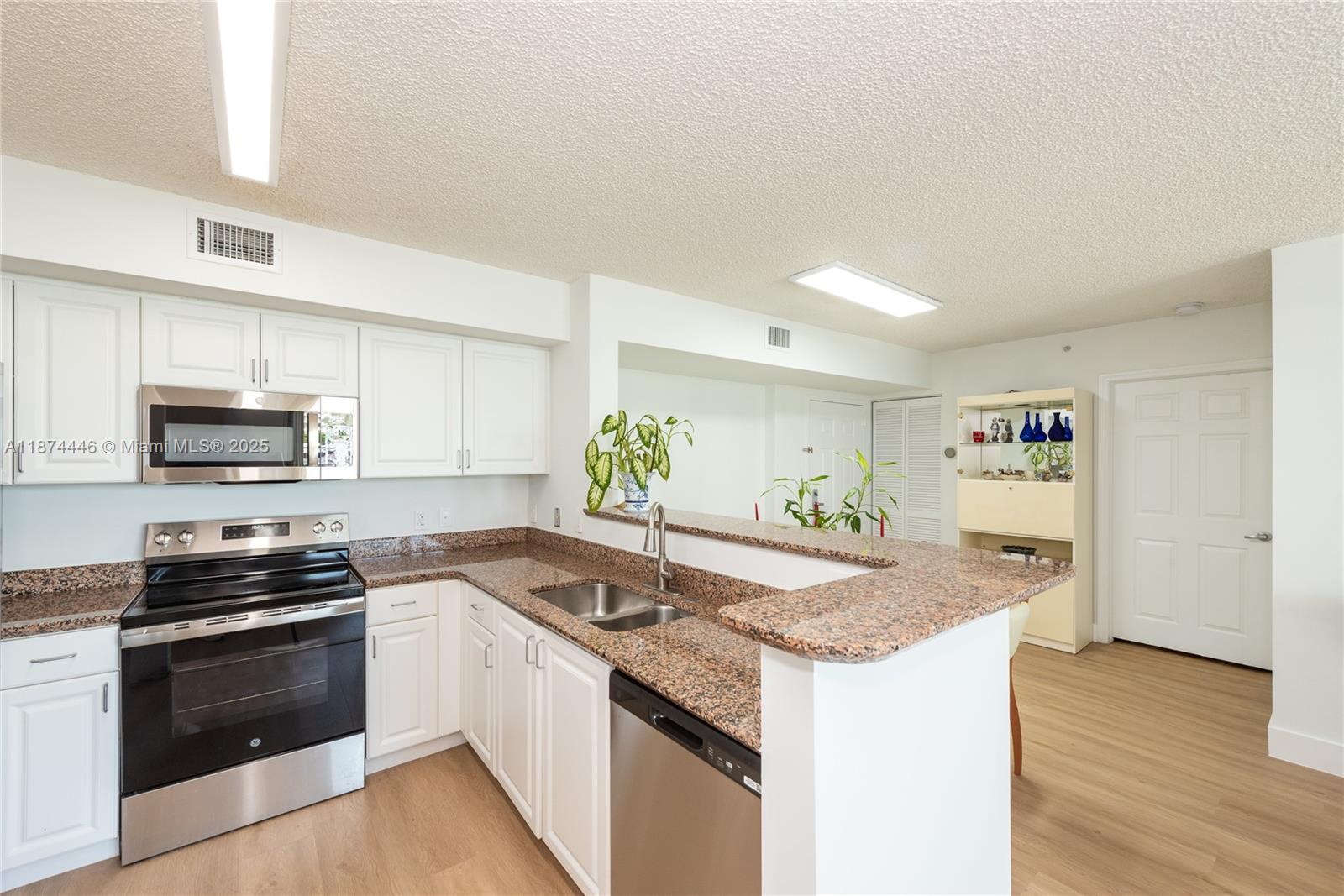 A kitchen features white cabinets, granite countertops, stainless steel appliances, and light wood flooring — 1155 Brickell Bay Dr # 609, Miami FL 33131, MIAMI, FL