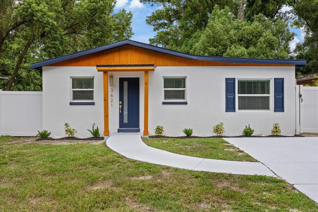 A single-story house with white stucco walls, a blue front door, and a wood-trimmed entryway — 3621 E COMANCHE AVENUE, TAMPA, FL