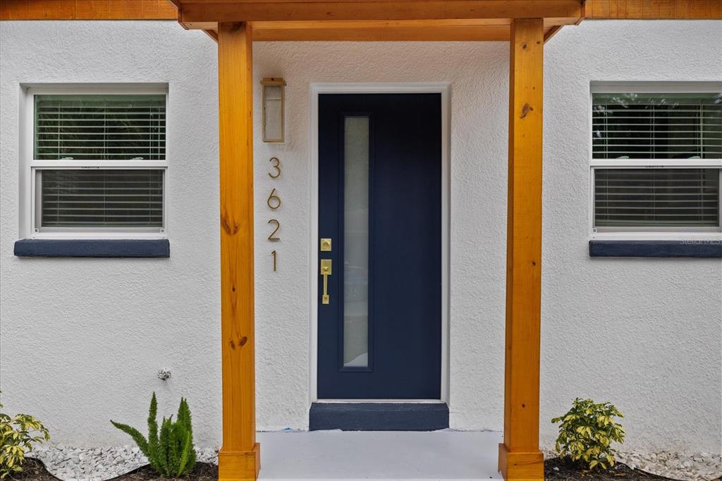 A dark blue front door with a vertical glass panel sits between two wooden posts — 3621 E COMANCHE AVENUE, TAMPA, FL