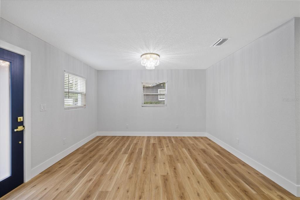 An empty room with light wood-look flooring, white walls, two windows, and a crystal chandelier — 3621 E COMANCHE AVENUE, TAMPA, FL