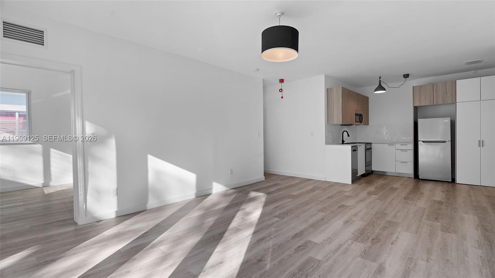 A bright, open-concept living area features light wood-look flooring and an adjacent modern kitchen — 1561 Jefferson Avenue, Miami Beach FL 33139, MIAMI BEACH, FL