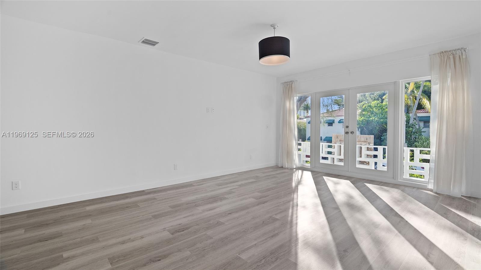 An empty room features light wood-look flooring, white walls, a black pendant light, and glass doors — 1561 Jefferson Avenue, Miami Beach FL 33139, MIAMI BEACH, FL
