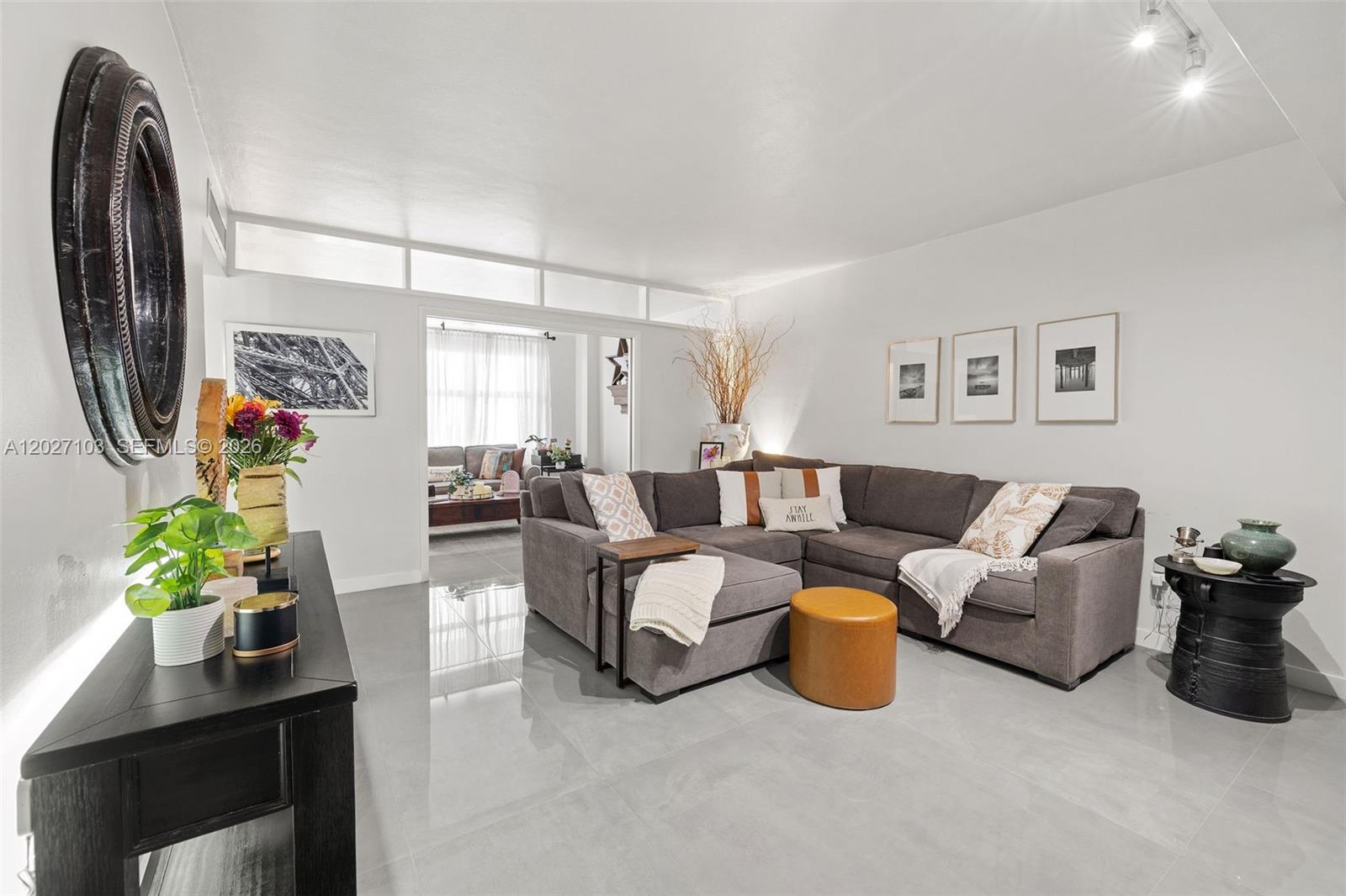 A living room features a gray sectional sofa, tiled floors, and a large circular wall mirror — 5001 Collins Ave # 1E, Miami Beach FL 33140, MIAMI BEACH, FL