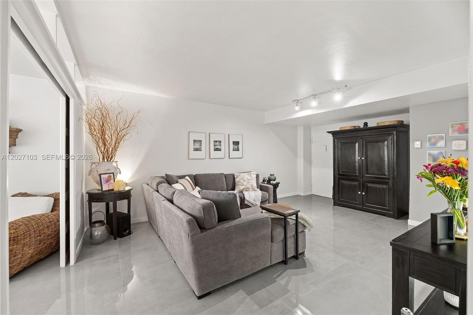 A living room features a gray sectional sofa, tile flooring, and a large dark wood cabinet — 5001 Collins Ave # 1E, Miami Beach FL 33140, MIAMI BEACH, FL