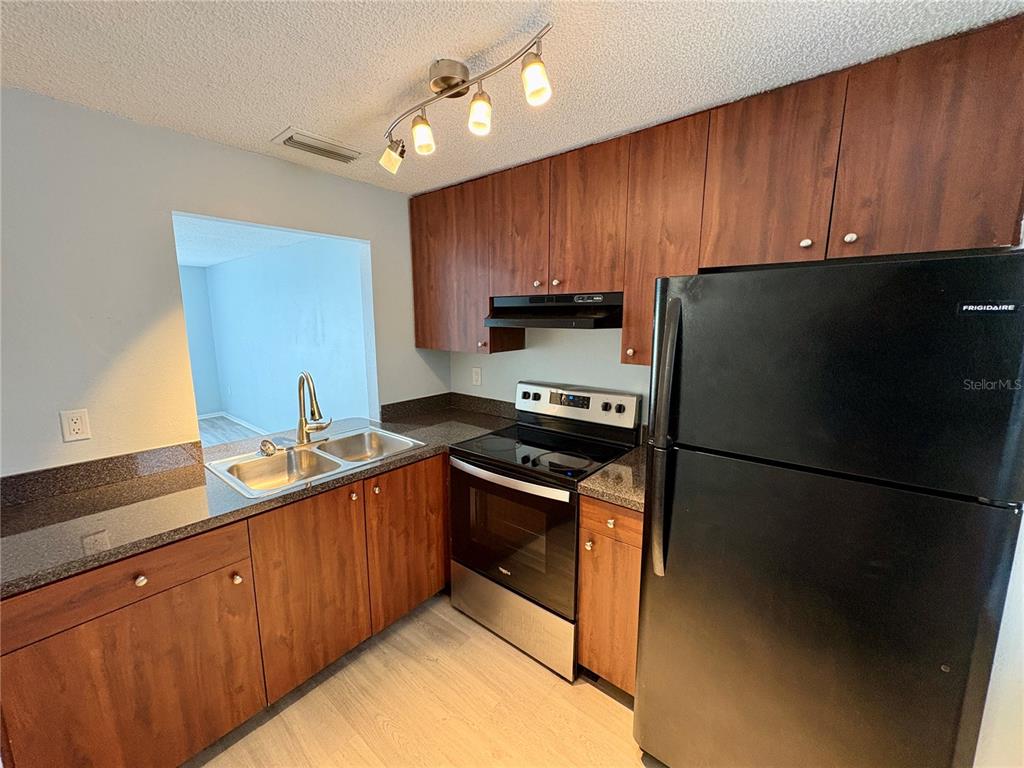 A kitchen features dark wood cabinets, granite countertops, stainless steel appliances, and a track light — 408 57TH AVENUE DRIVE E UNIT A, BRADENTON, FL