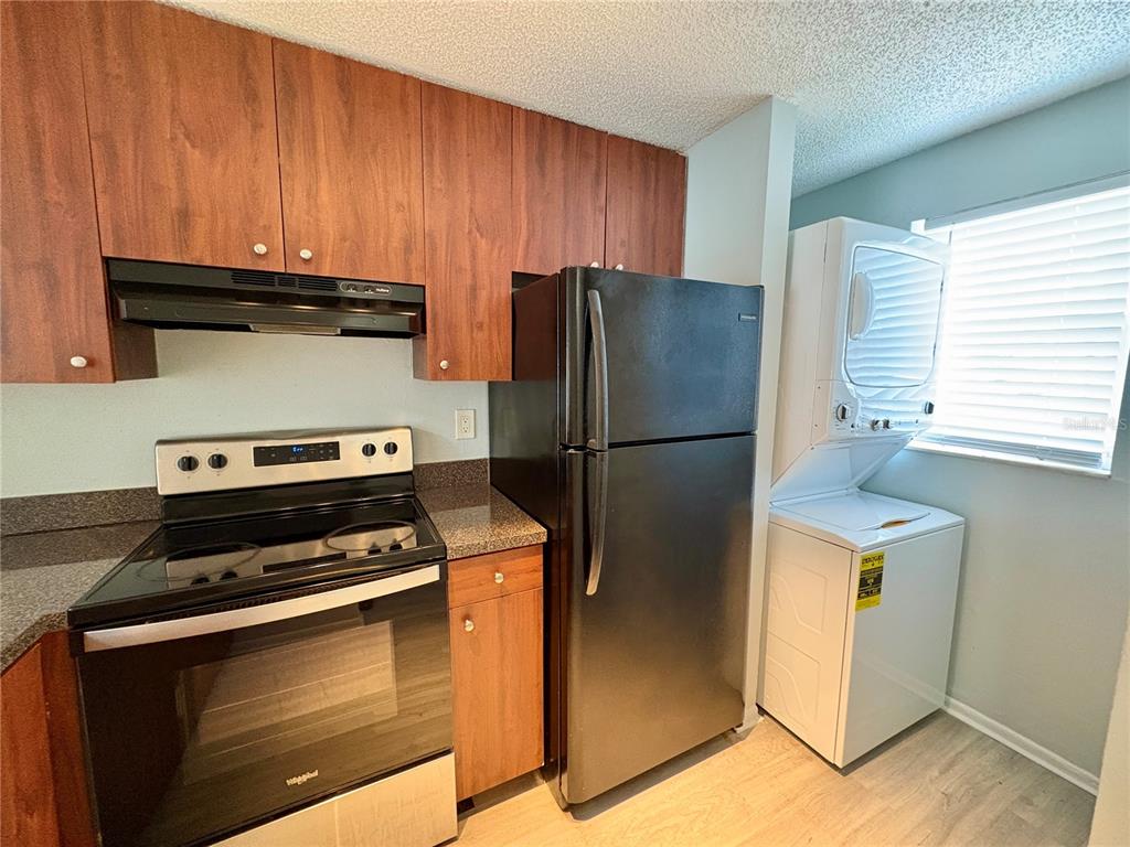 A kitchen featuring wood cabinets, black appliances, a stacked washer-dryer unit, and light flooring — 408 57TH AVENUE DRIVE E UNIT A, BRADENTON, FL