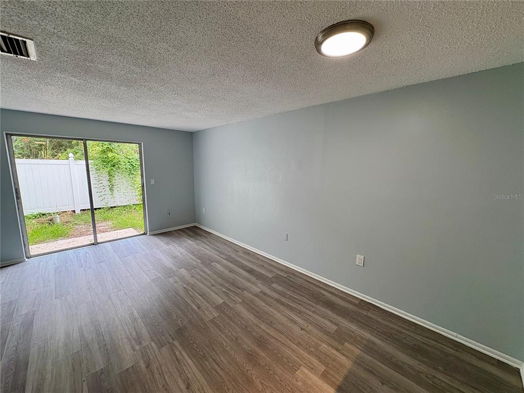An empty living room features light blue walls, wood-look flooring, and a sliding glass door — 408 57TH AVENUE DRIVE E UNIT A, BRADENTON, FL
