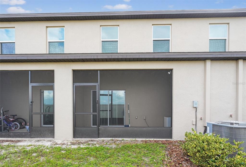 The exterior of a two-story townhouse features a screened-in patio and a small yard — 32021 POWDERPUFF MIMOSA DRIVE, SAN ANTONIO, FL
